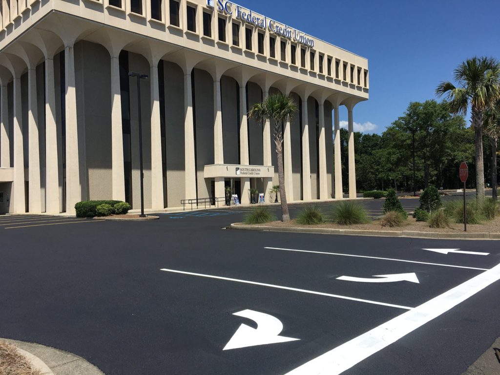 Bank parking lot with sealcoating and line striping. New white directional arrows.